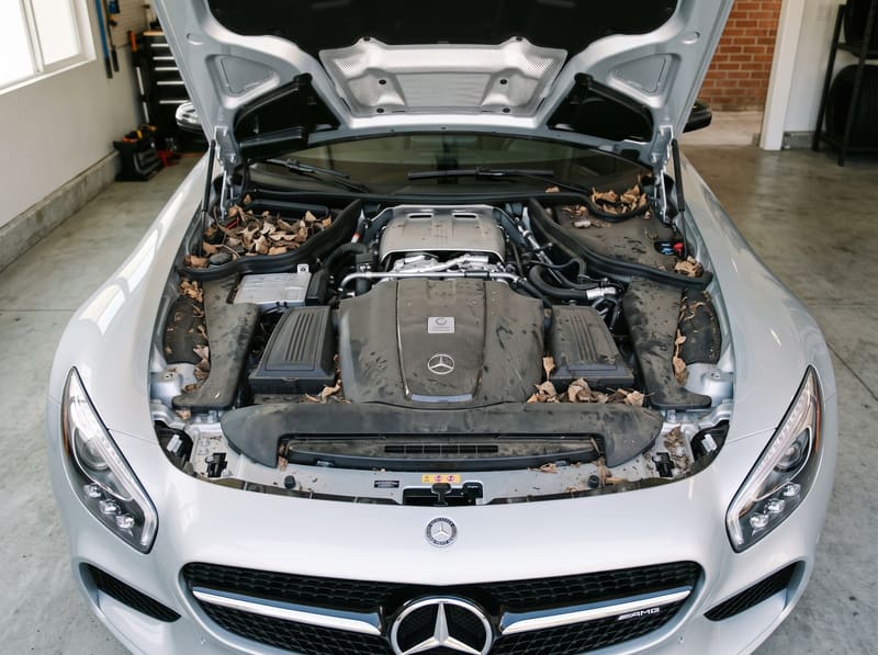 Engine bay wash in Los Angeles: the open engine bay of a silver Mercedes-AMG GT with dust, dry leaves and grime