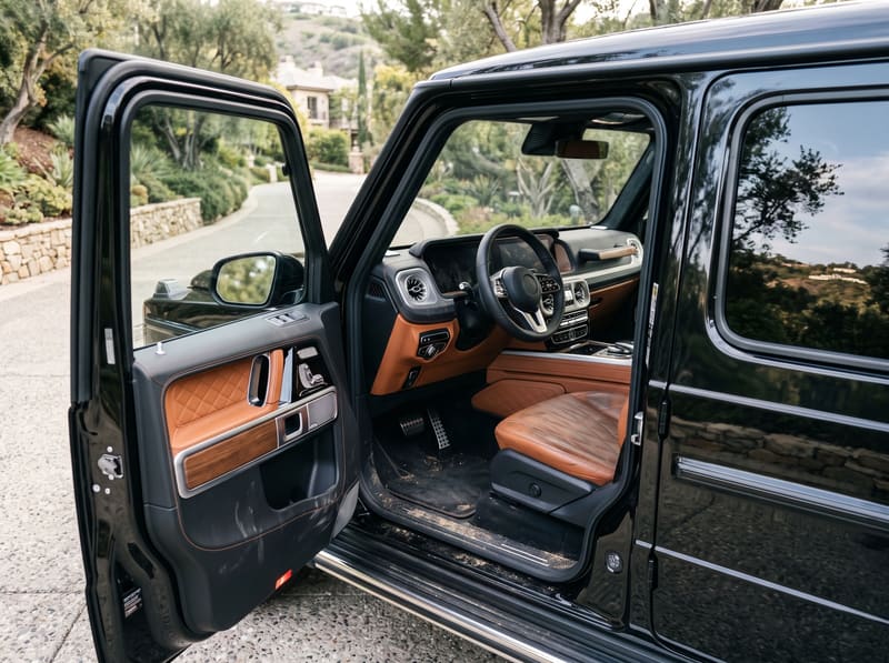 Interior car detailing in Los Angeles: the front cabin of a black Mercedes G-Class with grime in the cognac leather, sand on the carpet and dusty screens