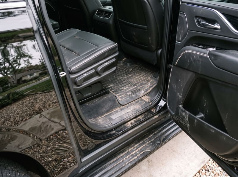 Mobile car shampoo in Los Angeles: the second-row carpet and mats of a black Cadillac Escalade with mud, sand, salt rings and a coffee stain
